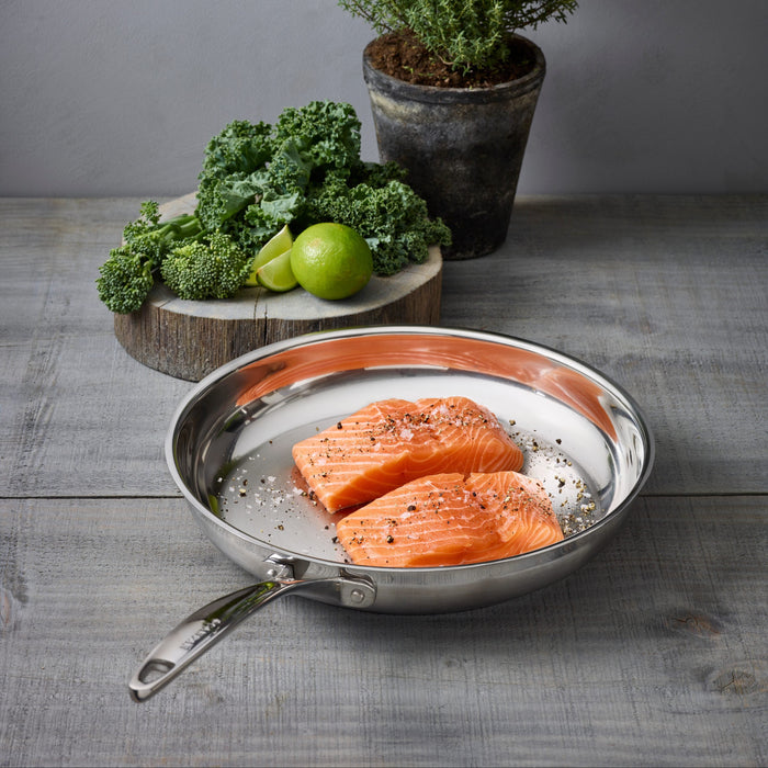 Raw salmon in a pan on a wooden table with greens and a plant in the background