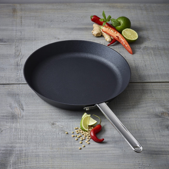 Black frying pan on a wooden surface with ingredients around
